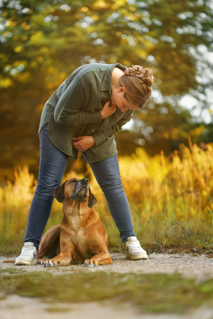 Hund-Mensch-Fotografie: Rhodesian Ridgeback zwischen den Beinen liegend von Frauchen